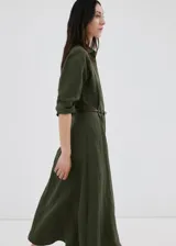 Vestido largo verde militar, con cuello camisero, cierre frontal con botones, mangas tres cuartos y diseño evasé. Incluye un cinturón fino de poliuretano con hebilla metálica.