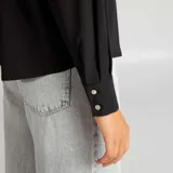 Camisa negra de corte holgado con cuello clásico y mangas largas con puños abotonados.