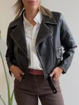 Campera estilo biker de ecocuero con cierre frontal cruzado, solapas amplias y detalles de costuras en contraste. Presenta bolsillos laterales con cierre y una tira ajustable en el ruedo.