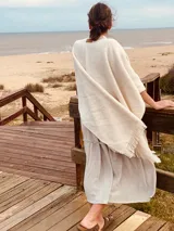 Ruana color crudo de tejido de punto grueso con flecos en el borde inferior.