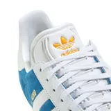 Championes adidas modelo Gazelle edición especial Real Madrid, confeccionados en gamuza azul con las icónicas tres tiras laterales en blanco. Presentan el nombre del club en letras doradas sobre el lateral y suela de goma blanca.
