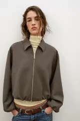 Chaqueta de corte corto y diseño abullonado en color marrón oscuro, con cuello solapa, mangas largas con puños elásticos y cierre frontal con cremallera metálica. Cuenta con bolsillos delanteros de doble vivo.