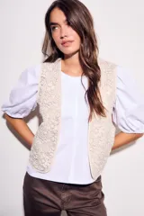 Chaleco sin mangas, color beige claro, con bordados florales en relieve y ribetes a contraste.