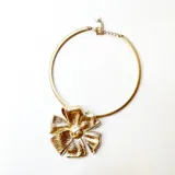 Gargantilla dorada rígida con dije desmontable de flor metálica.