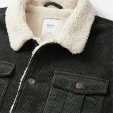 Campera de pana color negro con cuello y forro interior de borrego sintético. Presenta cierre frontal con botones metálicos, bolsillos de parche con solapa en el pecho y bolsillos laterales ribeteados.