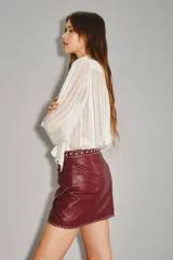 Falda corta cruzada de cuero ovino color bordó, con tachas metálicas plateadas decorando el borde y la cintura.