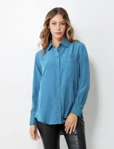 Camisa de satén color azul, con cuello clásico, cierre frontal con botones, manga larga con puños abotonados y bolsillo aplicado en el pecho.