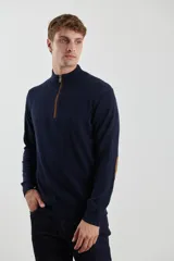 Sweater de punto gris con medio cierre frontal, cuello alto y coderas en tono marrón. Presenta un diseño clásico con puños y ruedo acanalados.