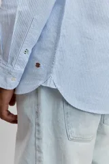 Camisa de manga larga en color celeste con estampado de rayas verticales finas, cuello abotonado y cierre frontal con botones.