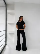 Pantalón oxford negro de tiro bajo, con detalle de doble cinturón con ojales metálicos y hebilla grande circular plateada.