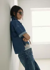 Blusa de algodón estilo denim, con diseño oversize, cuello camisero, mangas cortas, dos bolsillos de parche en el pecho y cierre frontal de botones.