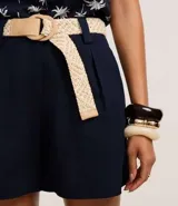 Short recto de cintura alta color crudo, confeccionado en viscolino, con trabillas en la cintura, pliegues y cierre tradicional. Incluye cinturón de rafia artificial con hebillas de argollas.