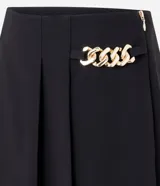 Short pollera de sastrería marca Cortelle, color bordó, confeccionado en crepé. Presenta sobreposición frontal efecto pollera con pliegues y detalle de cadena metálica decorativa en el lateral.