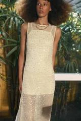 Vestido midi de cuello redondo y sin mangas, confeccionado en tejido de red con lentejuelas brillantes. Presenta un diseño con forro interior corto, aberturas laterales en el bajo y cierre de botón en la espalda.