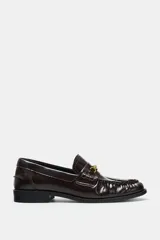 Mocasín plano de mujer con acabado acharolado color bordó. Presenta un diseño con fruncidos en el empeine y una hebilla metálica dorada decorativa. Cuenta con punta redonda y suela plana de 2,5 cm.