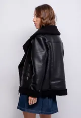 Campera tipo gamulán de símil cuero color marrón oscuro, con interior y solapas de corderito al tono. Presenta cierre frontal cruzado, bolsillos con cierre metálico y hebilla ajustable en el cuello.