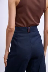 Pantalon de vestir de corte recto y tiro alto, confeccionado en tela de lino en color beige. Presenta pinzas frontales, cierre con botón y detalle de vivos en contraste en la cintura.