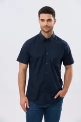Camisa lisa de algodón azul marino, de manga corta, con cuello camisero, cierre frontal de botones y un bolsillo aplicado en el pecho.