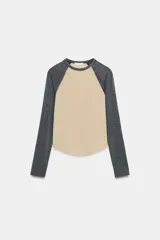 Camiseta de manga larga tipo ranglán con cuello redondo. Presenta un diseño bicolor con cuerpo en tono beige y mangas en gris jaspeado, con bajo redondeado.