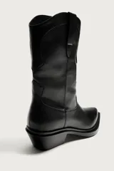 Bota estilo cowboy de color negro, con acabado liso, tiradores laterales, horma en punta, suela a tono y tacón ancho.