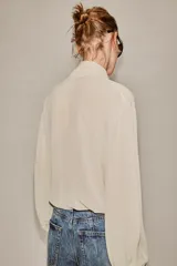Camisa de manga larga con escote en pico y detalle de lazada frontal en el mismo tejido. Presenta puños abotonados y bajo asimétrico.