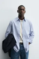 Camisa de corte regular fit confeccionada en tejido de algodón con estampado de rayas verticales. Presenta cuello abotonado, manga larga con puños abotonados y cierre frontal de botones.