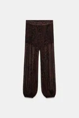 Pantalón bombacho de tiro medio, color marrón oscuro con estampado animal print negro. La tela es semitransparente y presenta un efecto plisado o texturizado. El bajo de la pierna termina en un puño elástico.