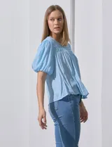 Blusa blanca de gasa marca Zac & Rachel, con frunces en la parte delantera, mangas cortas con puño elastizado, abertura central en la espalda y botón.