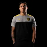 Remera deportiva Puma del Club Atlético Peñarol, con diseño de bloques de color gris en la parte superior y negro en la parte inferior. Presenta detalles en amarillo en los hombros, logo de la marca y escudo del club en el pecho.