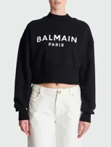 Sweatshirt negro Balmain Paris de corte cropped, con cuello alto y logo estampado en blanco. Presenta botones dorados en el hombro.