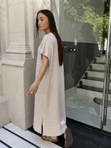 Vestido largo de tejido de punto con diseño de rayas verticales en blanco y negro. Presenta escote en V, mangas cortas y tajos laterales en el ruedo para mayor movimiento.