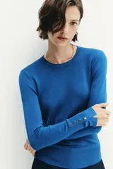 Jersey Zara de punto liso color negro, con cuello redondo, manga larga y detalle de botones dorados en los puños.