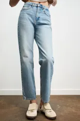 Jeans de mujer, tiro alto, color azul medio con efecto desgastado (lavado claro en muslos y oscuro en bordes). Corte recto y ancho (mom fit) con cinco bolsillos y cierre frontal de botón y cremallera.