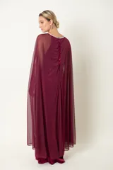 Vestido largo de fiesta color granate, confeccionado en terciopelo con cuello redondo adornado con strass y capa de chifón que nace de los hombros.