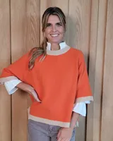 Buzo de lana lambswool color naranja con cuello, puños y ruedo en tejido acanalado color beige. Presenta un diseño holgado con mangas tres cuartos y aberturas laterales.