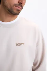 Buzo de corte oversize en color visón, con cuello redondo y puños acanalados. Presenta un diseño estampado en la espalda con tipografía y gráficos en tono marrón.