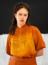 Blusa color ocre de algodón tipo seda, teñida a mano con técnica tie dye. Tiene corte recto, cierre invisible en el escote delantero y mangas regulables con elástico.