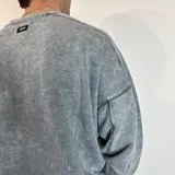 Buzo de cuello redondo con corte oversize, confeccionado en tela con efecto lavado ácido. Presenta costuras reforzadas visibles y una pequeña etiqueta con logo en el puño.