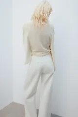 Camiseta tipo capa oversize de color blanco, confeccionada en hilatura de algodón 100%. Presenta cuello redondo, manga corta y un diseño de bajo asimétrico con caída pronunciada en uno de los laterales.