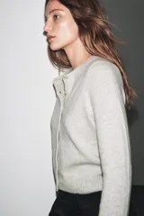 Chaqueta de lana 100% color gris claro, con cuello redondo, manga larga y cierre frontal con botones.