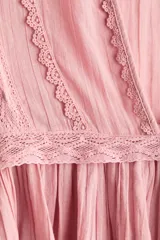 Blusa rosada de algodón con ribetes de encaje, cuello redondo con abertura en V y tiras para anudar, mangas largas abullonadas con puños elásticos y terminación peplum con vuelo.