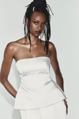 Top palabra de honor de tejido satinado blanco, con escote recto y diseño con bajo tipo peplum y costuras marcadas.