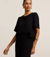 Blusa negra de mangas cortas abullonadas, confeccionada en tejido airflow con textura arrugada y abertura en forma de gota en la espalda.