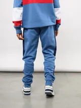 Pantalon de jogging azul de felpa, con franjas laterales en blanco y azul marino. Presenta el escudo del Club Nacional de Football en el muslo derecho y el logo de Umbro en el izquierdo.