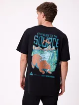 Remera de corte oversize color negro, con estampa gráfica en la espalda que presenta un oso, un paisaje montañoso y el texto 'Stay close to the source'.