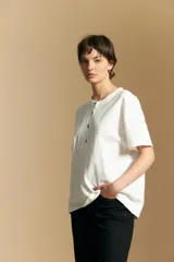 Remera de manga corta color marrón, con cuello redondo y cierre frontal parcial con botones. Presenta un diseño de calce relajado y líneas simples.