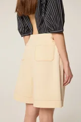 Bermuda de tiro alto en color crudo, confeccionada en lona de algodón. Presenta un corte acampanado con pliegues en la cintura, bolsillos delanteros inclinados y costuras decorativas en contraste color camel.