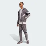 Chaqueta deportiva Adidas del Real Madrid en color gris, con diseño de bloques en blanco y azul marino, cuello alto, cierre frontal y las icónicas tres tiras en las mangas.