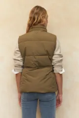 Chaleco puffer color crema, con cuello alto, cierre frontal y cuatro bolsillos con solapa. Cuenta con cintura ajustable con cordón.