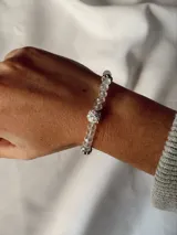 Pulsera elástica compuesta por cuentas de cristal transparente, con una cuenta central blanca decorada con strass y separadores brillantes.